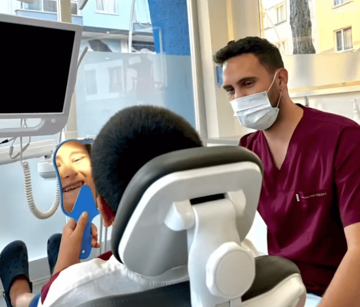 Ein Zahnarzt in Kitteln lächelt, während er einen jungen Patienten in einer Zahnarztpraxis untersucht